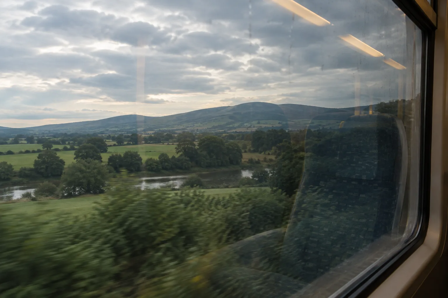 Le reflet discret d’un siège se superpose à un paysage de campagne vu du train.