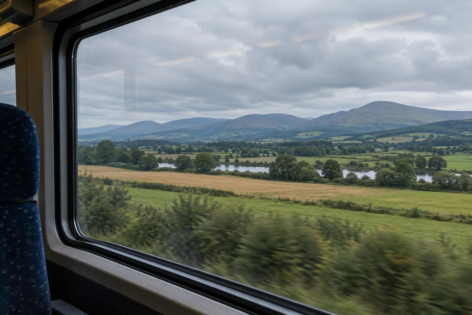 Des champs et des collines se reflètent légèrement dans la vitre d’un train.