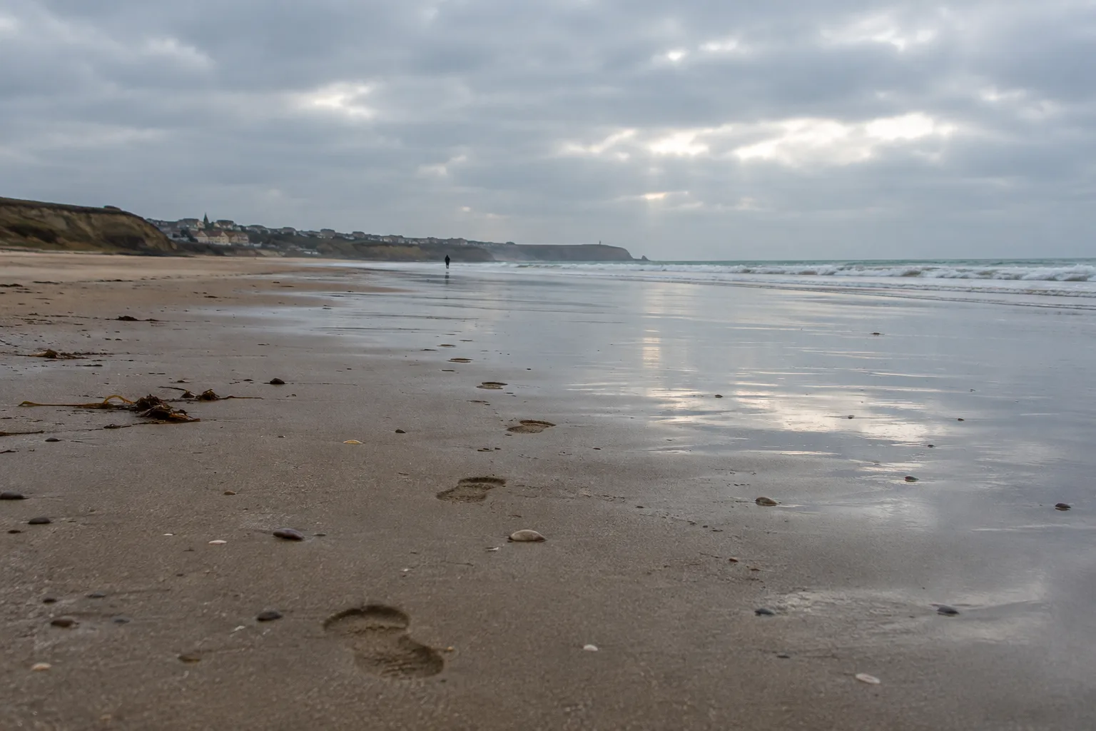 Des empreintes dans le sable conduisent vers le rivage d’une plage calme hors saison.
