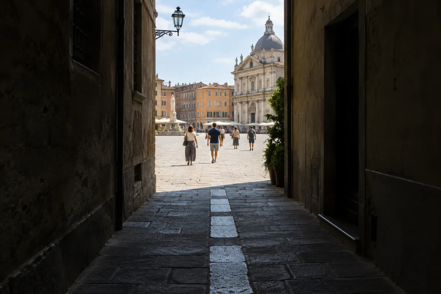 Depuis une ruelle sombre, une place ensoleillée apparaît au bout des pavés.